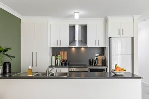 A modern kitchen with white cabinets, stainless steel appliances, and a central island. - Stylish and Spacious Launceston Villa + Free Wifi (Launceston)