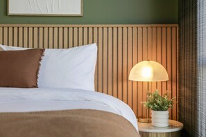 A neatly made bed with a white and brown blanket, a wooden headboard, a bedside lamp, and a small potted plant on a bedside table. - Stylish and Spacious Launceston Villa + Free Wifi (Launceston)
