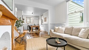 A spacious living room with a large window, a dining area with a wooden table, and a beige sofa.