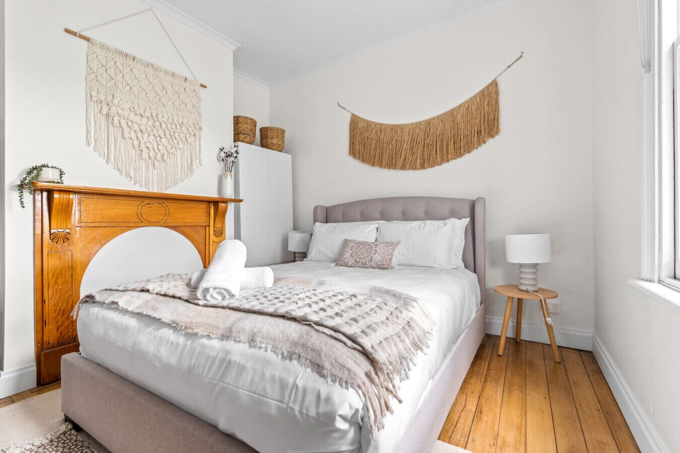 A bedroom with a bed, a wooden nightstand, a hanging macrame wall hanging, and a woven wall hanging.