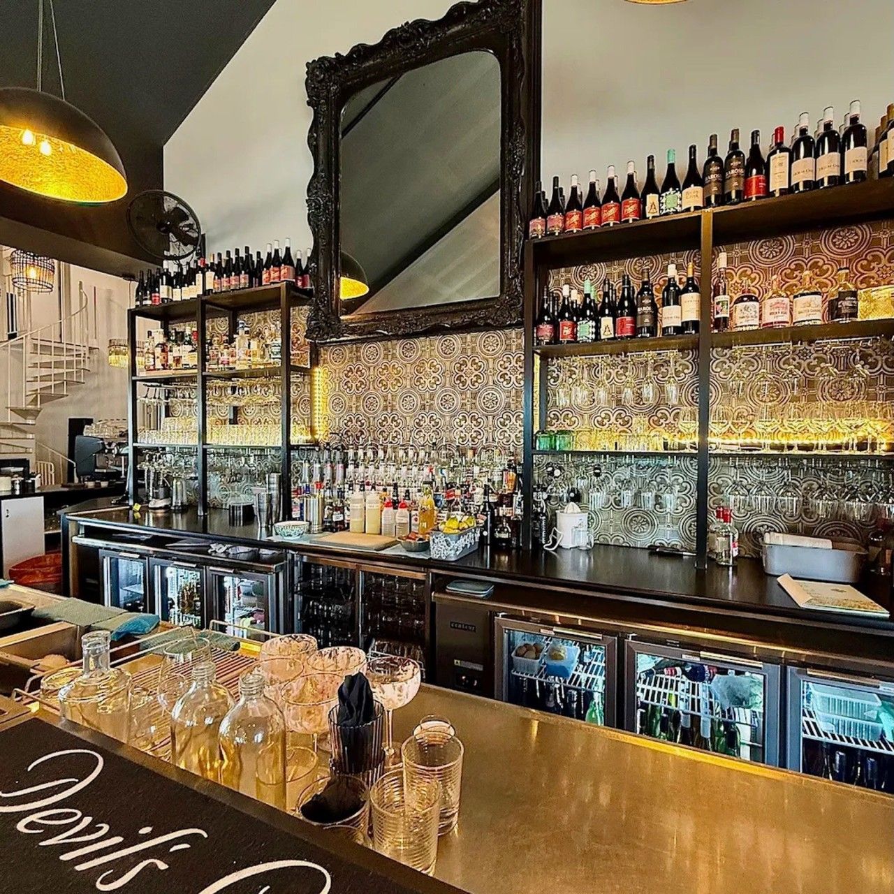 En bar med flasker på hylder, en bardisk med glas og et dekorativt spejl.