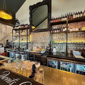 Zona de bar amb prestatges plens de botelles, un taulell amb gots i un mirall decoratiu.