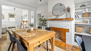 A dining area with a wooden table, black chairs, a white brick fireplace, and a mirror above it.