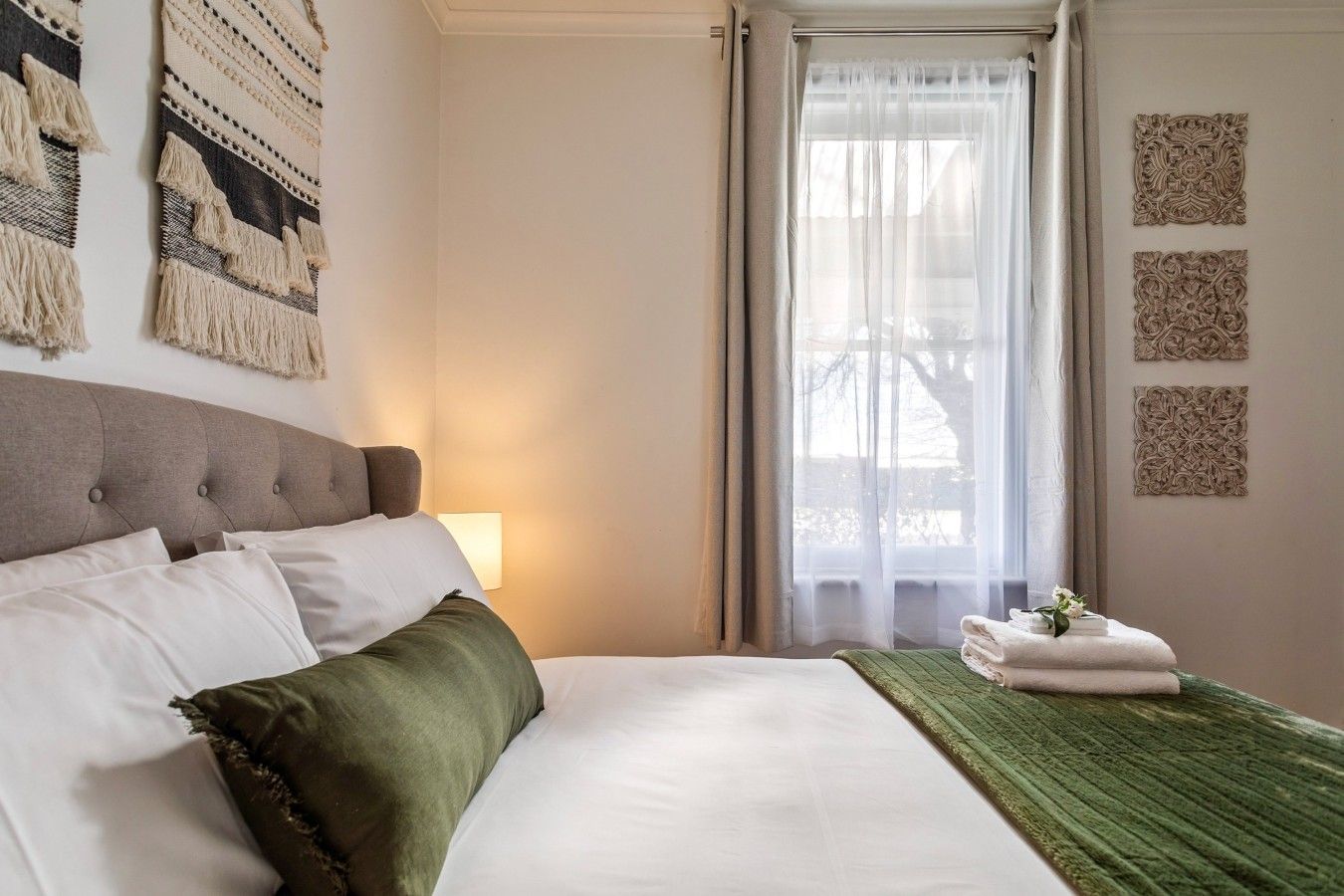 Ein Hotelzimmer mit Bett, Lampe, Fenster mit Vorhängen und dekorativer Wandgestaltung.