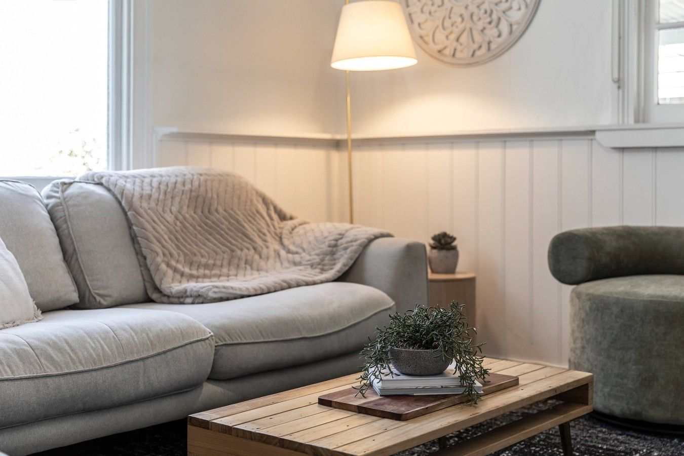 Ein Wohnzimmer mit einer Couch, einem Couchtisch mit einer Pflanze, einer Lampe und einem Sessel.