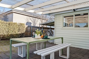 A patio with a table and benches, a potted plant, and a bottle of wine.
