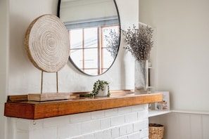 A fireplace mantel with a mirror, a wooden bowl, and a vase with dried flowers.