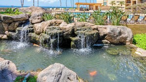 Un área de piscina en un resort, con una cascada, palmeras y vistas al océano.