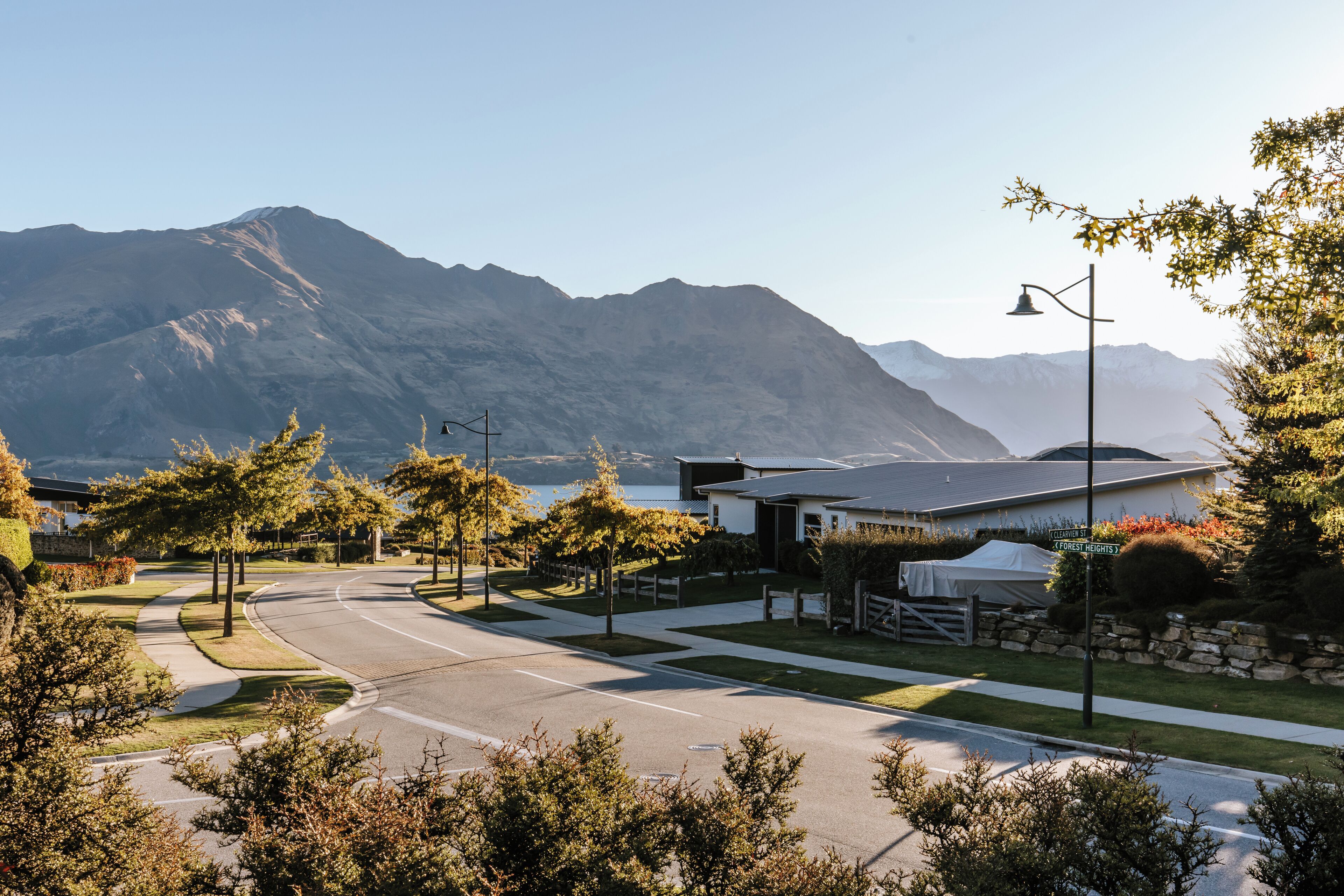 A residential area with a curved road, houses, a white tent, and mountains in the background.