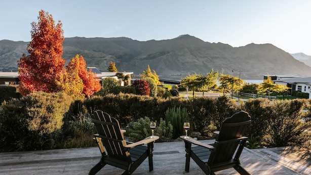 A wooden deck with two Adirondack chairs and a small table, overlooking a mountainous landscape with autumn foliage. - The Clearview House - Lake Views (Wanaka)