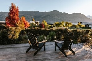 Eine Holzterrasse mit zwei Adirondack-Stühlen und einem kleinen Tisch, mit Blick auf eine gebirgige Landschaft im Herbstlaub.