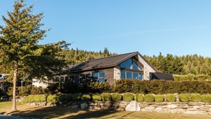 A modern house with a stone facade, large windows, and a well-maintained lawn. - The Clearview House - Lake Views (Wanaka)