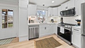 Una cocina moderna con armarios blancos, electrodomésticos de acero inoxidable y un ventanal que proporciona luz natural.