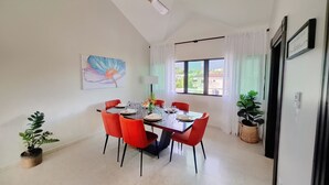 A dining area with a table set for six, red chairs, a ceiling fan, a window with curtains, and a painting on the wall. - Spacious 2BR, Fast WiFi/Ocean & Mountain Views, Security & Convenience (Puerto Plata)