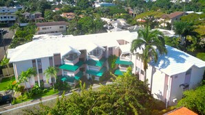 A multi-story building with a flat roof, surrounded by greenery and palm trees. - Spacious 2BR, Fast WiFi/Ocean & Mountain Views, Security & Convenience (Puerto Plata)