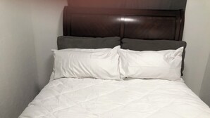 A bed with a white quilted bedspread and two pillows, one white and one gray, against a dark wooden headboard. - Anchors Way Inn (Anchorage)