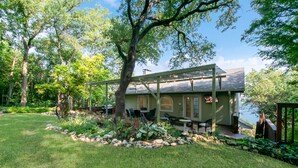 Una casa con porche cubierto, césped y jardín con rocas y plantas.