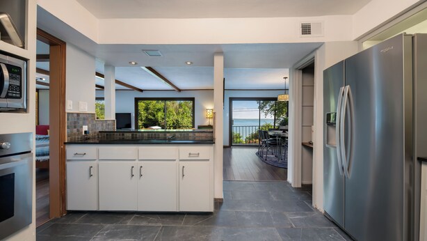 Una cocina moderna con armarios blancos, un refrigerador de acero inoxidable y un amplio ventanal con vistas a la vegetación.