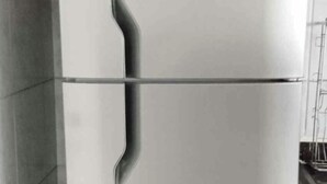 A stainless steel refrigerator with a digital display, located in a kitchen with tiled walls and a stainless steel sink.