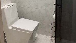 A bathroom with a white toilet, a glass shower enclosure, and marble-patterned tiles.