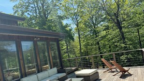 A wooden deck with wicker furniture and a glass enclosure. - Chronogram featured, Modern Mountain Family Home above Woodstock. Dog-Friendly (Bearsville)