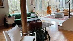 A spacious living room with wooden beams, a green sofa, a white armchair, and a grand piano. - Chronogram featured, Modern Mountain Family Home above Woodstock. Dog-Friendly (Bearsville)