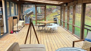 A wooden deck with a sofa, a table, and a telescope. - Chronogram featured, Modern Mountain Family Home above Woodstock. Dog-Friendly (Bearsville)