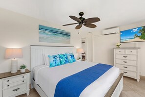 A bedroom with a bed, nightstands, a dresser, a ceiling fan, a TV, and a painting of a beach scene.