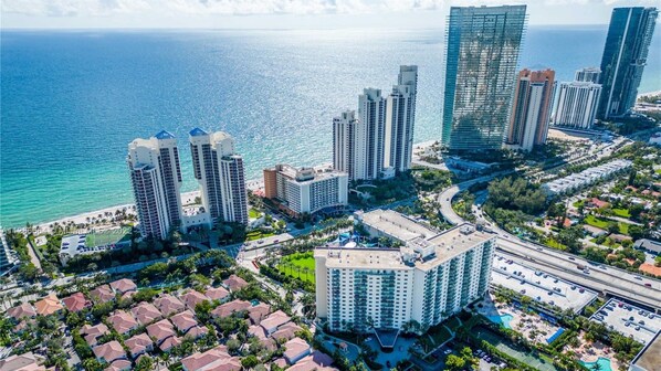 A coastal cityscape with high-rise buildings, a marina, and a residential area with houses and a swimming pool.