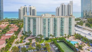 A high-rise hotel with multiple floors, a swimming pool, and a tennis court.