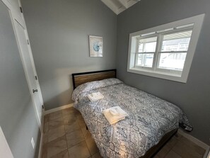 A bedroom with a bed, a window, a door, and a wall-mounted picture.