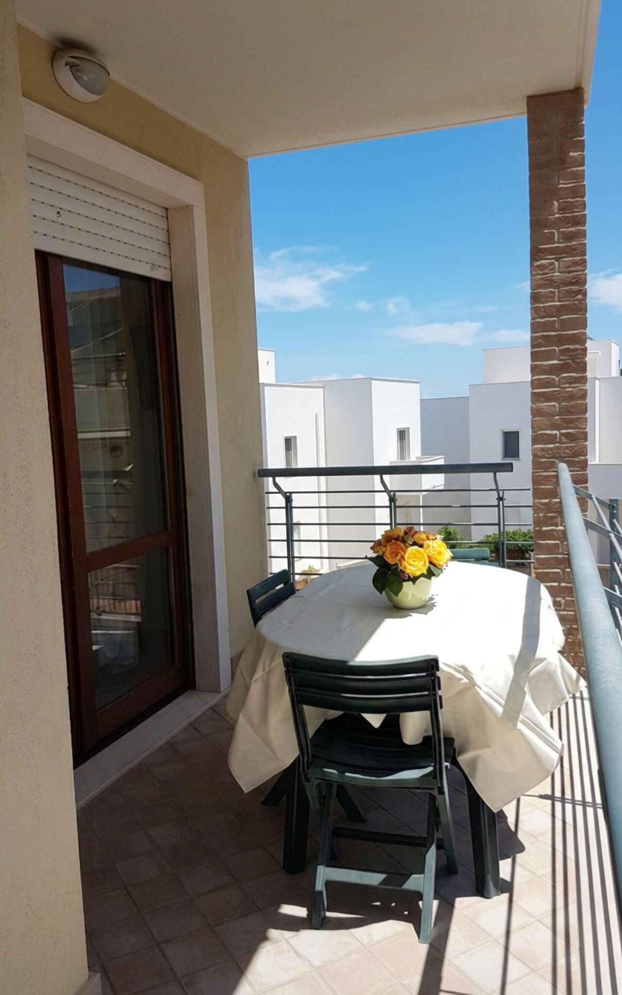 A balcony with a table, chairs, and a vase of flowers.
