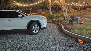 A white SUV parked on a gravel driveway at night, surrounded by trees and string lights.
