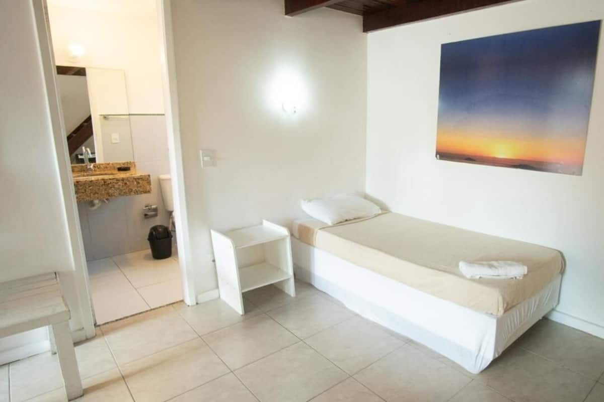A small, clean room with a bed, a nightstand, a chair, and a painting on the wall.