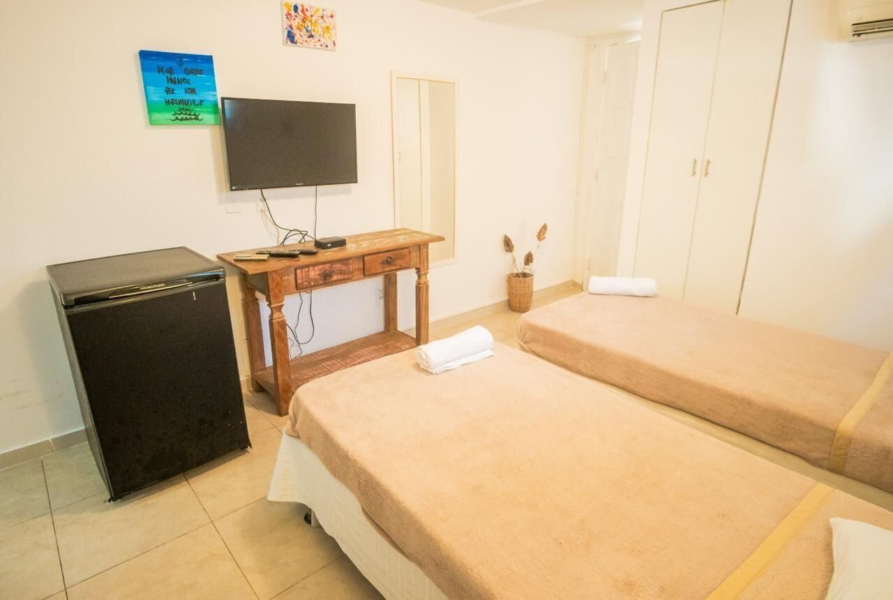 Una habitación con dos camas, televisión, escritorio, refrigerador y armario.