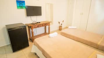 Una habitación con dos camas, televisión, escritorio, refrigerador y armario.