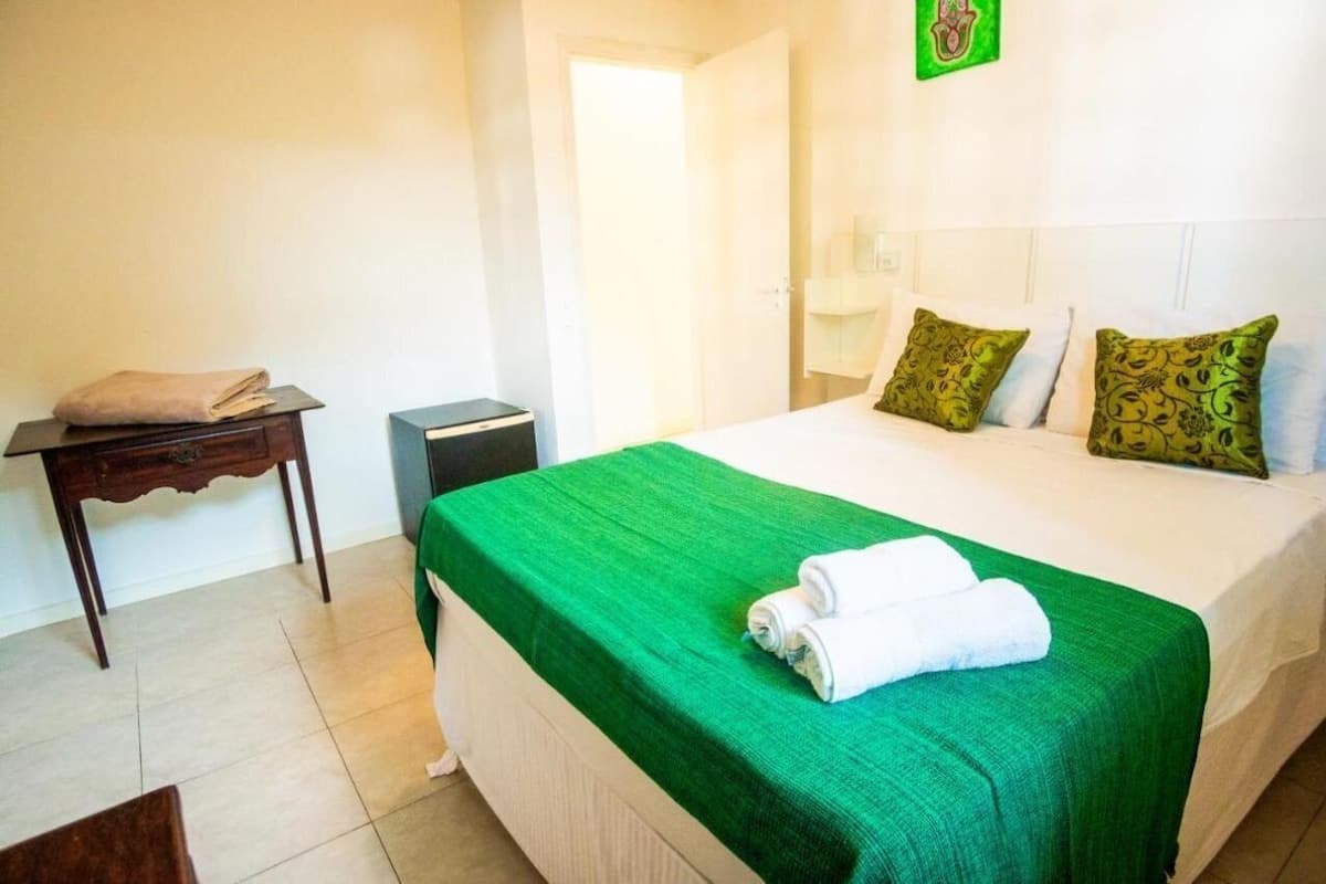 A hotel room with a bed, a nightstand, a green bedspread, and a towel on the bed.