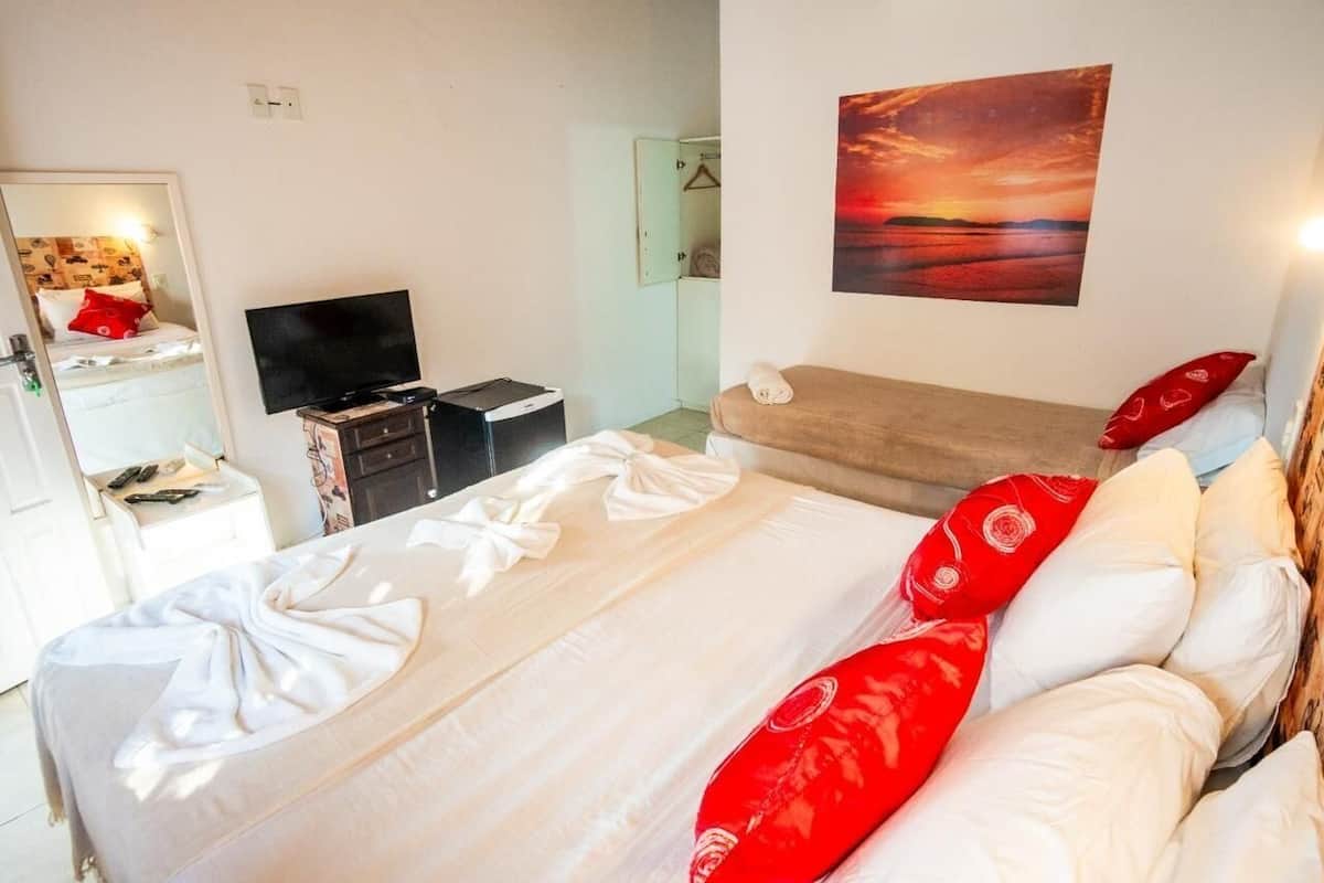 A hotel room with a bed, a TV, a desk, and a painting of a sunset.