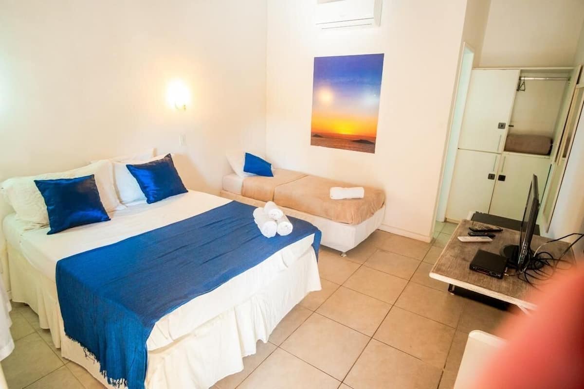A bedroom with a bed, a desk, and a chair. There is a painting on the wall and a window.