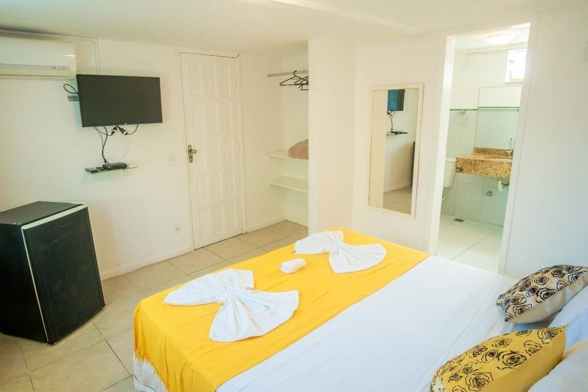 A hotel room with a bed, a TV mounted on the wall, a small black speaker, and a mirror.