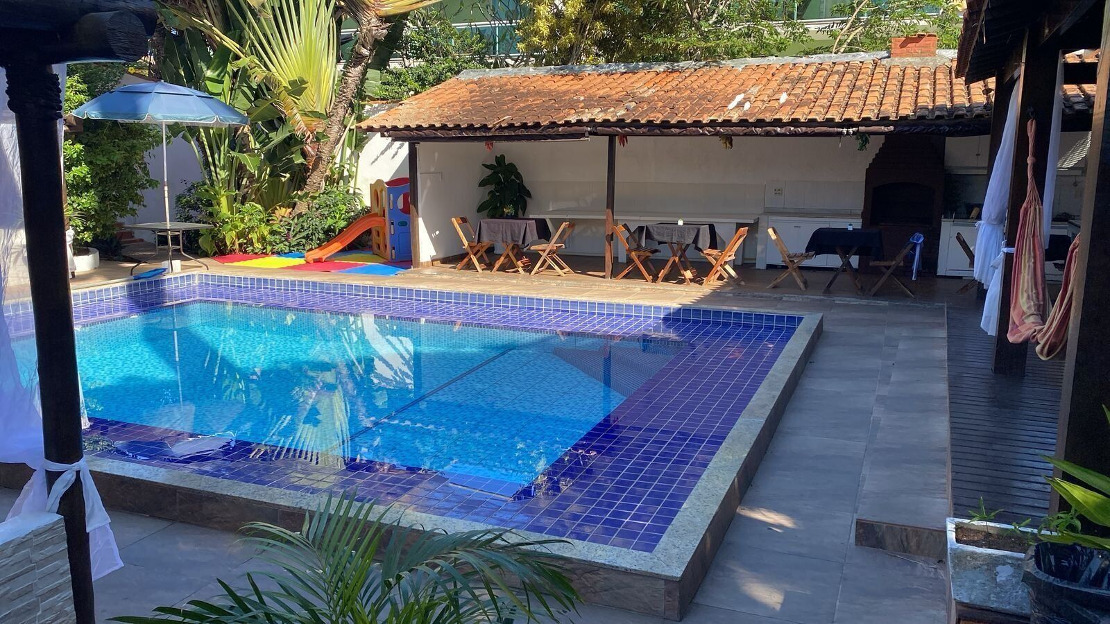 A swimming pool with a tiled deck, surrounded by lounge chairs and a small play area with slides.