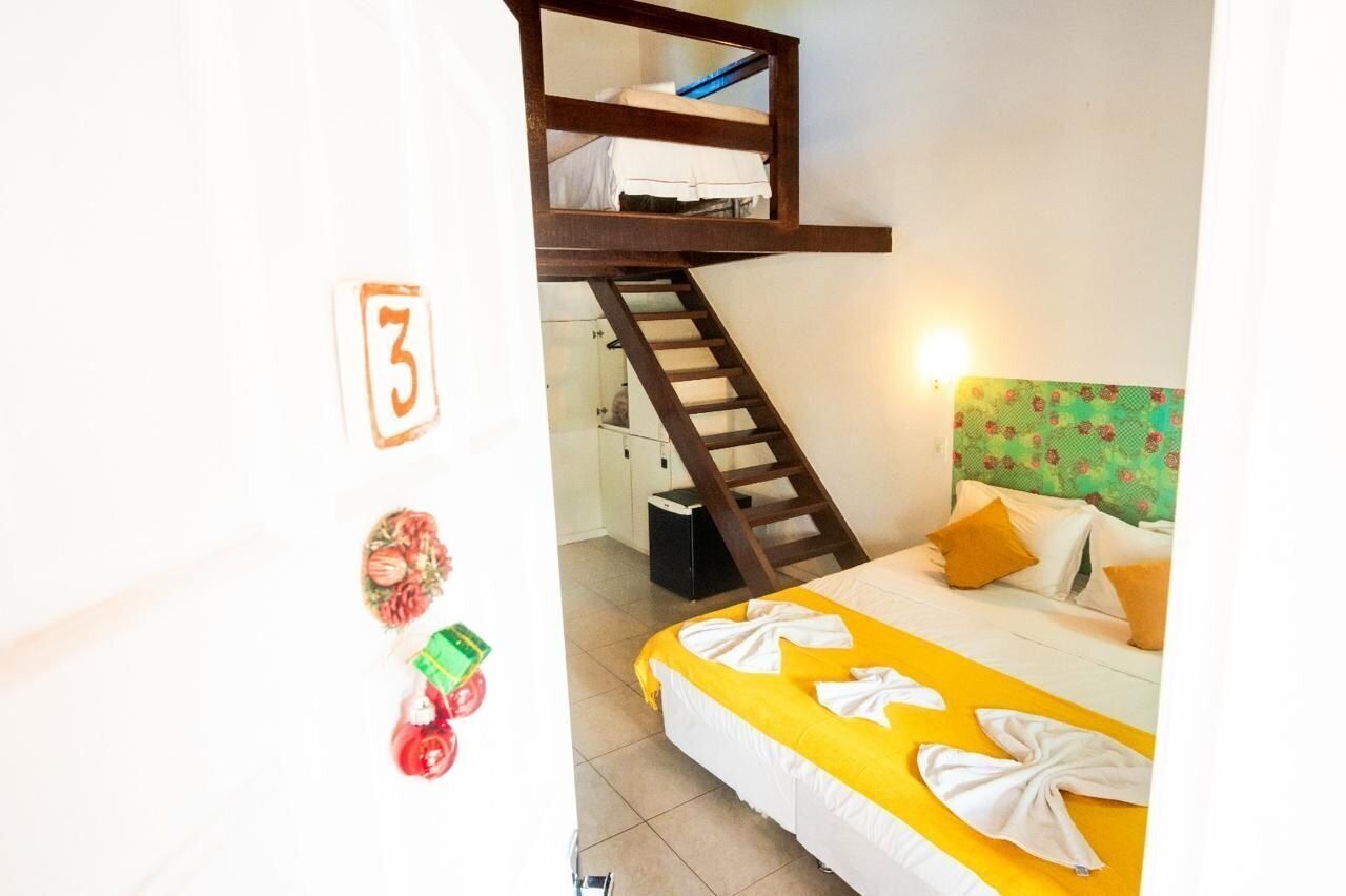 A hotel room with a bunk bed, a staircase, a bed with yellow and white bedding, and a green floral headboard.