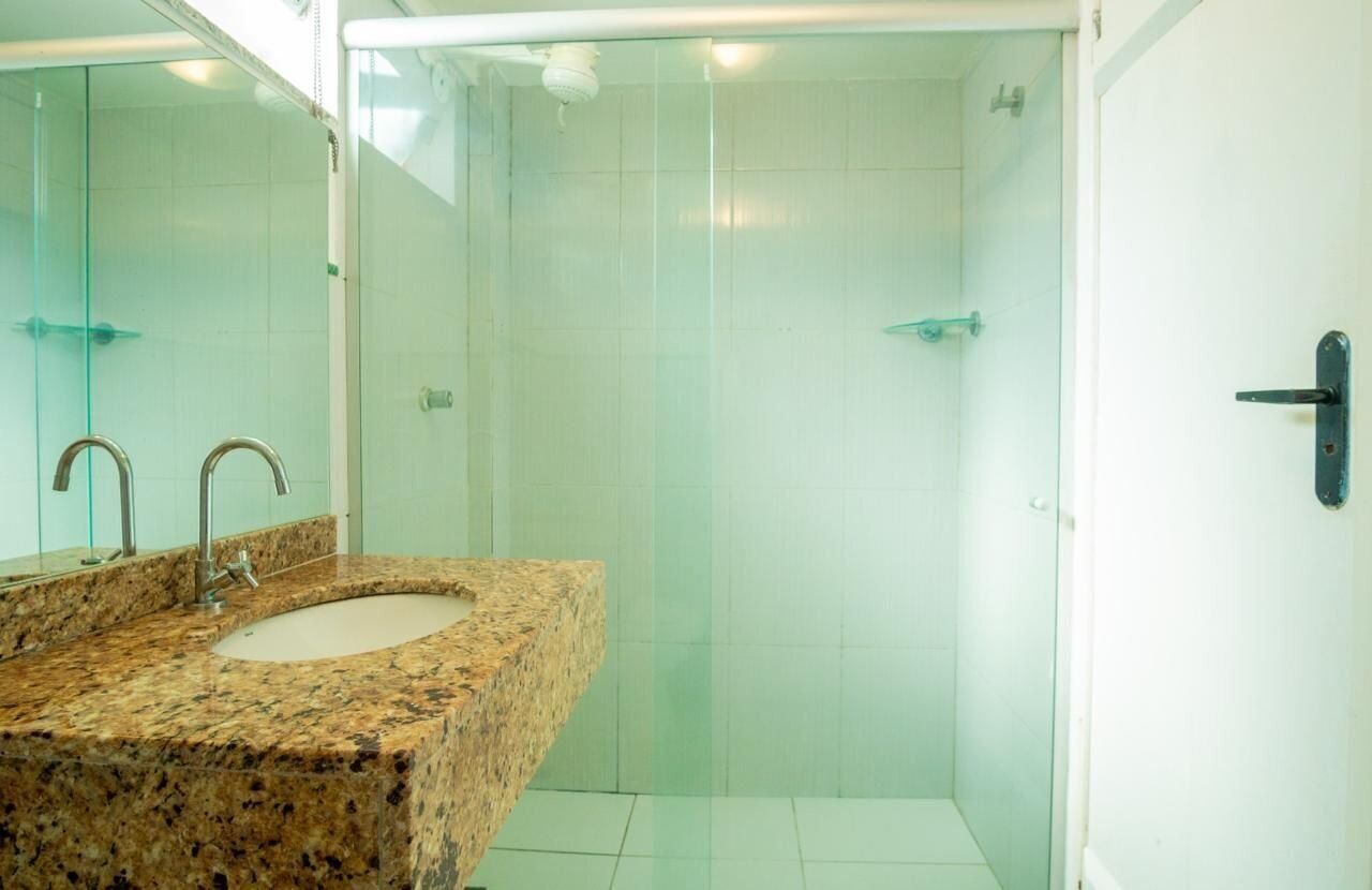 A bathroom with a granite sink, a mirror, a glass shower enclosure, and a white tiled wall.