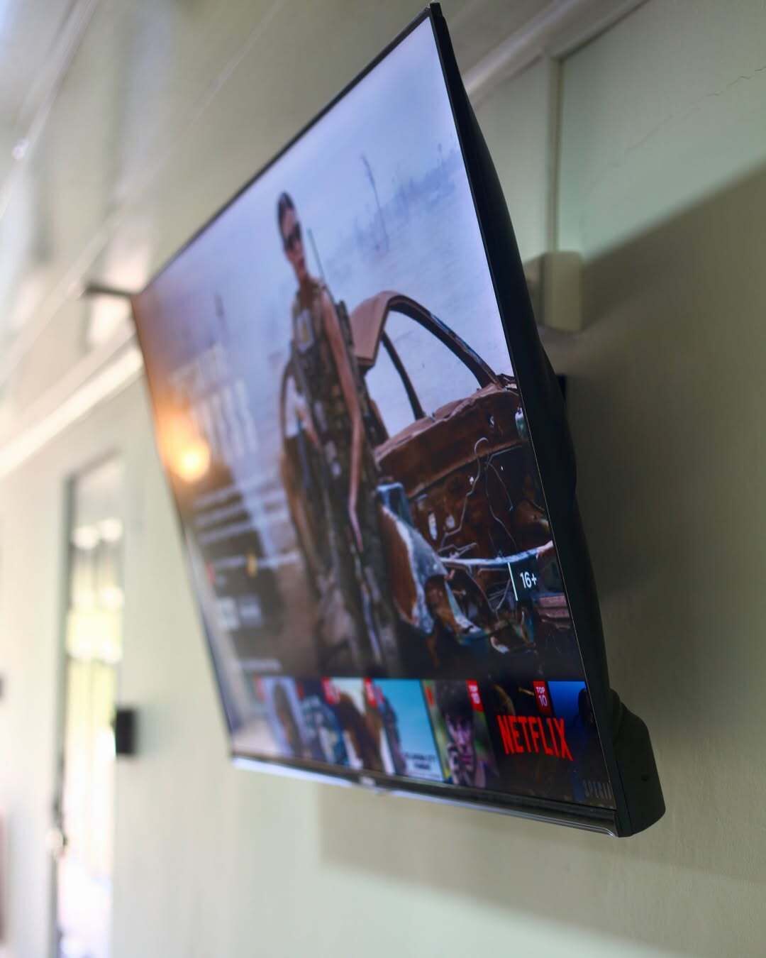 A television mounted on a wall displaying a movie with a '16+' rating and the Netflix logo.