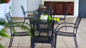 A dining area with a table and chairs, a kitchen in the background, and a tiled floor.