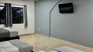 A hotel room with two beds, a flat-screen TV mounted on the wall, and a window with curtains.