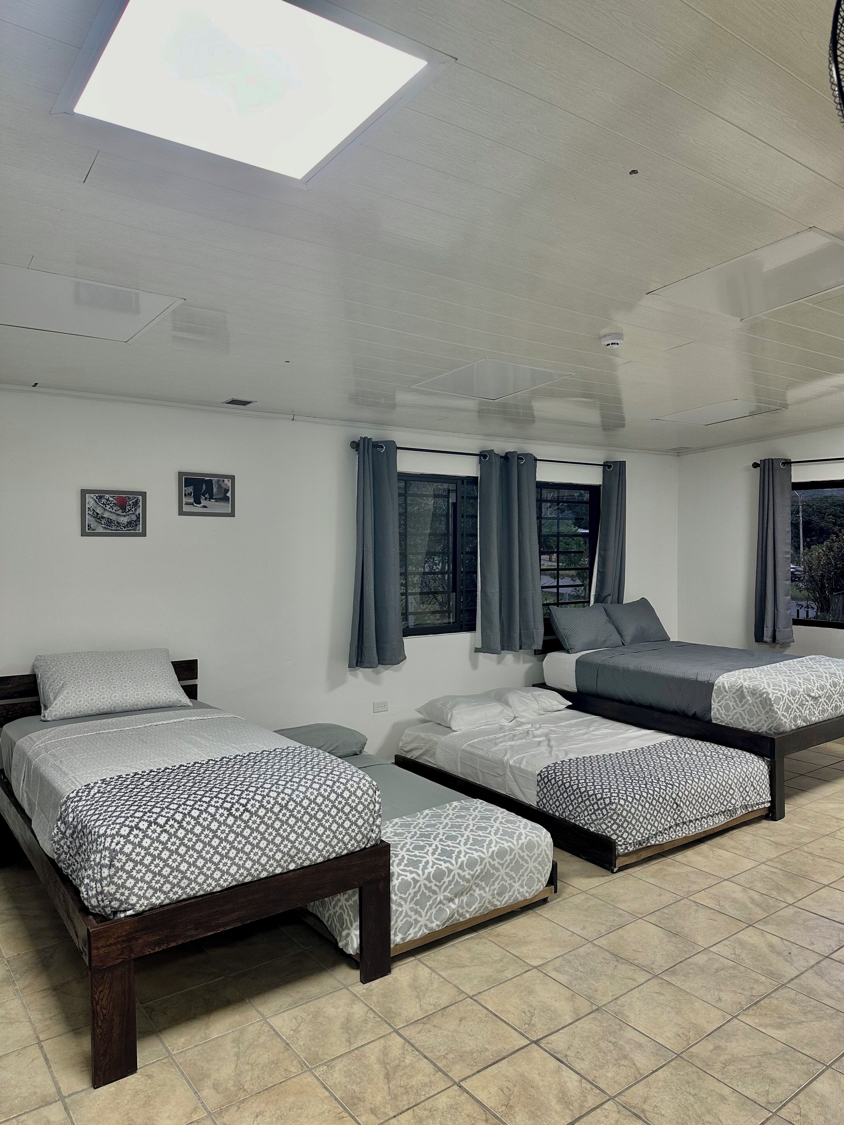 Une chambre avec trois lits, une lucarne et une fenêtre avec des rideaux.