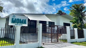 A white building with a sign reading "MOMA GUEST HOUSE" and a gated entrance.