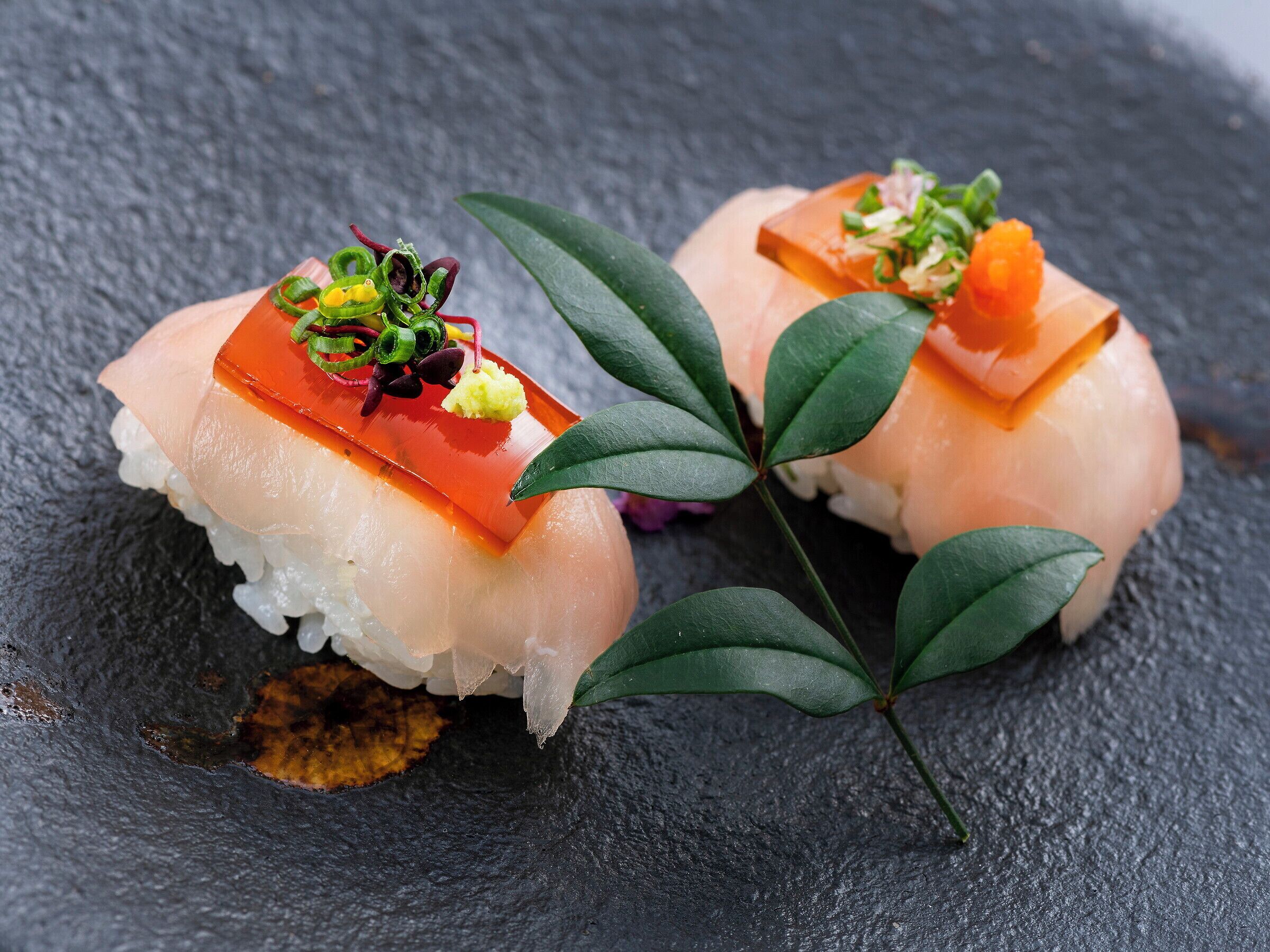 Two sushi pieces on a dark slate surface with green leaves.