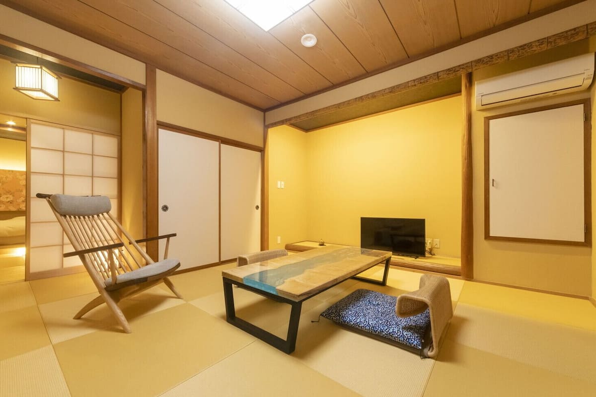 A traditional Japanese room with tatami flooring, a low table, a television, and sliding doors.